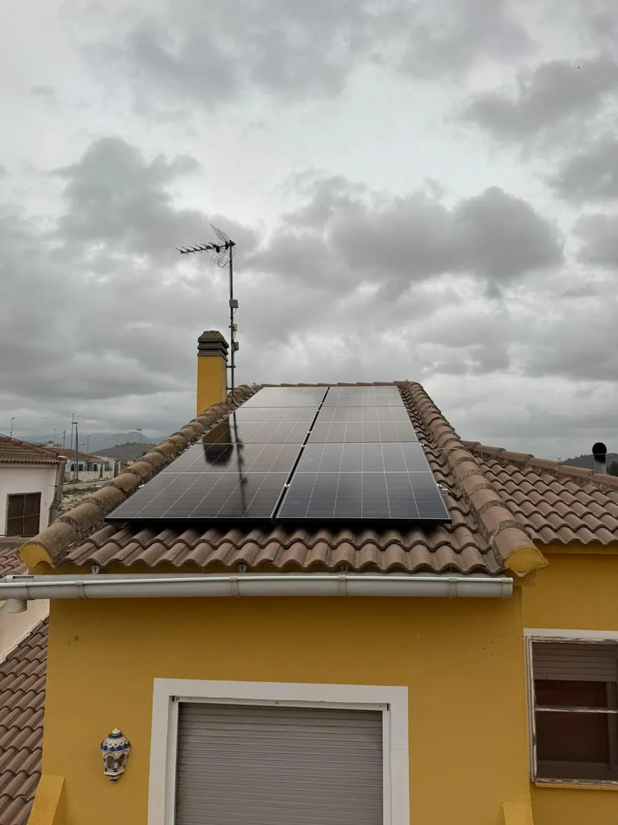 Paneles fotovoltaicos sobre el tejado de una vivienda de fachada amarilla